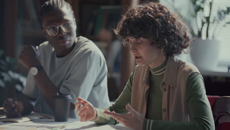 girl sitting at table and talking to classmates during college lesson