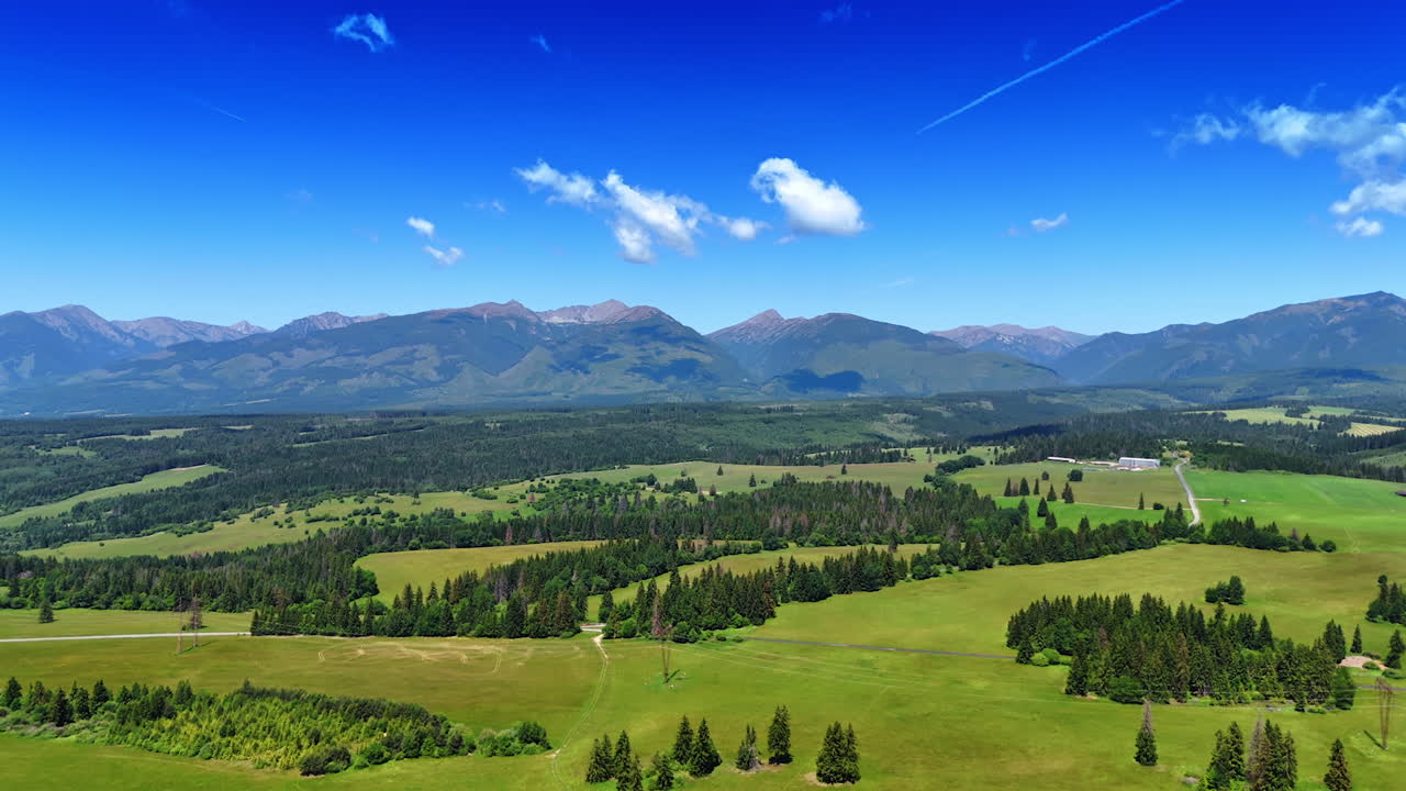 Flight above the valley with meadows and woods in Slovakia. Beautiful mountain range of Tatras at backdrop