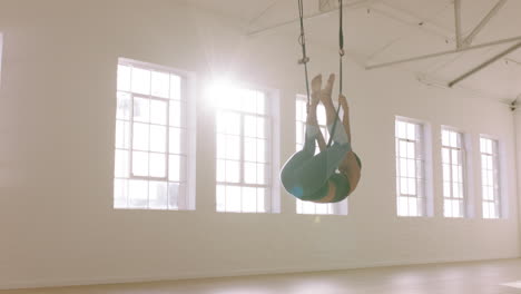 aerial yoga woman practicing inverted butterfly pose hanging upside down using hammock enjoying healthy fitness lifestyle exercising in studio training meditation at sunrise