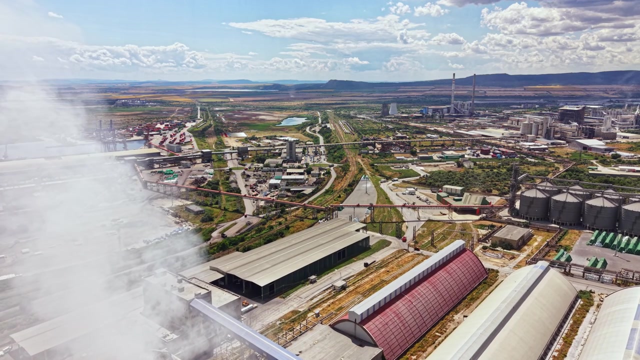 Vista de una gran zona industrial con fábricas y humo en el aire, tomada desde arriba durante el día con nubes en el cielo
