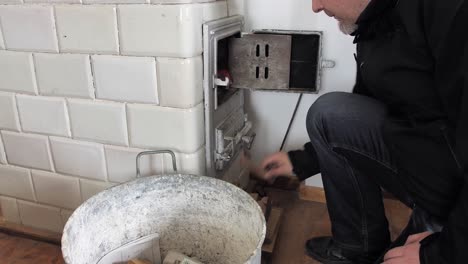 el hombre pone leña a través de la puerta abierta en la vieja estufa de azulejos