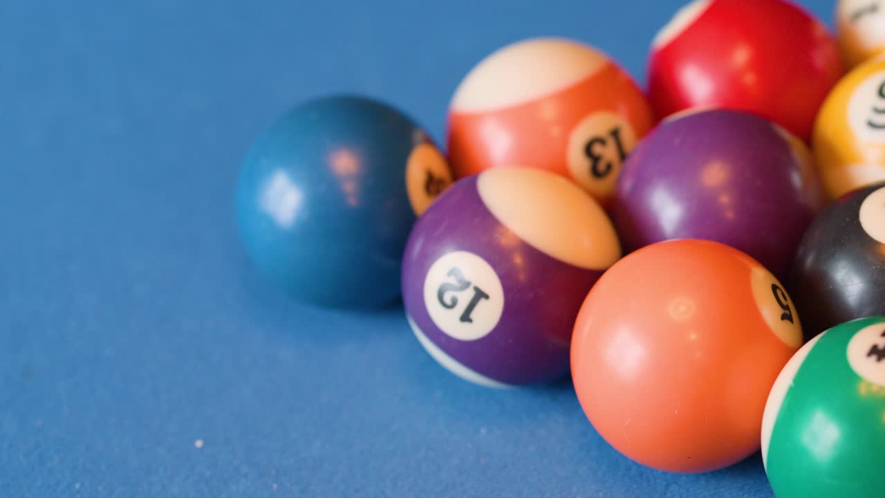 Numbered billiard balls roll across a blue felt pool table under soft, even lighting conditions
