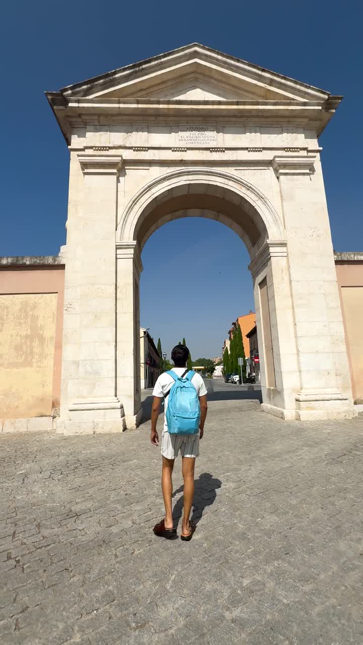 Turista che cammina attraverso la Puerta de Madrid ad Alcalá sotto un cielo azzurro