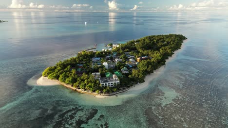 Aerial-drone-shot,-panning-around-the-small-local-island-of-Thinadhoo-during-sunrise-in-the-Vaavu-Atoll,-Maldives