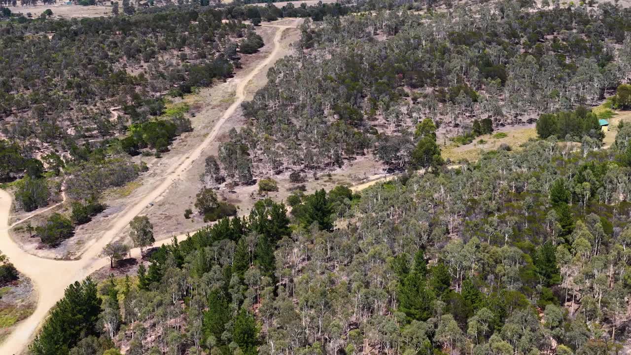 Droneoptagelse i høj engel panorerer hen over tørt australsk bushland og snoede mountainbike-stier af jord.