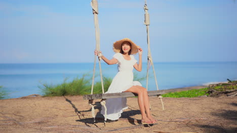 young woman with big straw hat on swing and sea in background