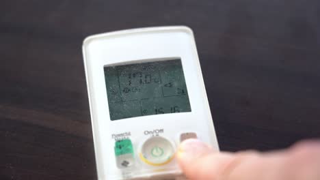 reducción de la temperatura ambiente en el control remoto de la bomba de calor mientras se coloca sobre la mesa - dedo borroso en primer plano con la temperatura en el control remoto enfocado