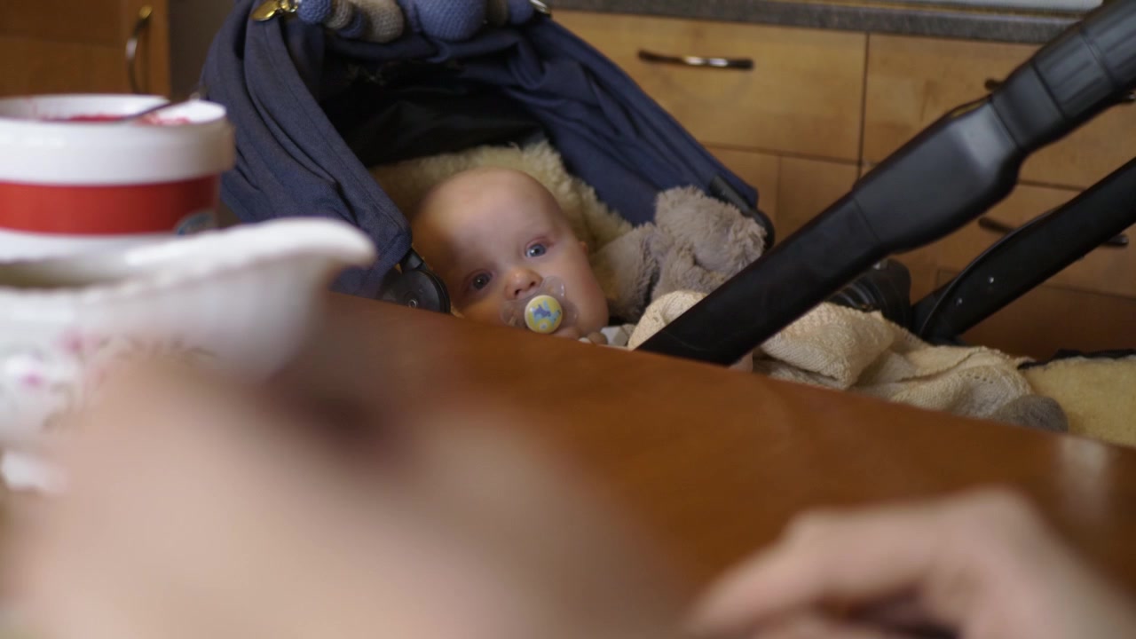 Baby in pram staring at mother eating at dinner table bokeh shallow focus