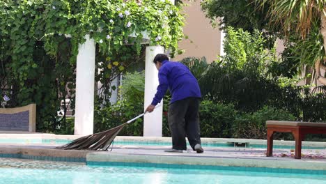 person sweeping leaves by a swimming pool