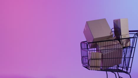 video of boxes and shopping trolley with copy space over neon purple background