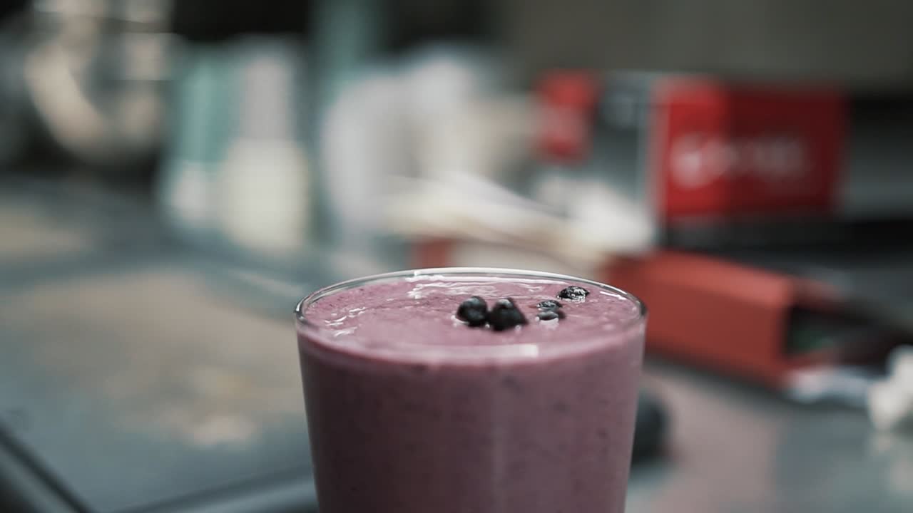 Hand adds blueberries and drinking straw into milkshake. Handheld
