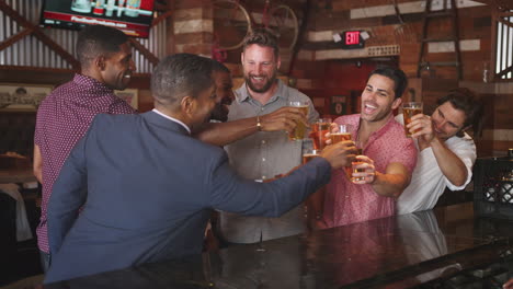 group of male friends on night out drinking beer at bar together making a toast