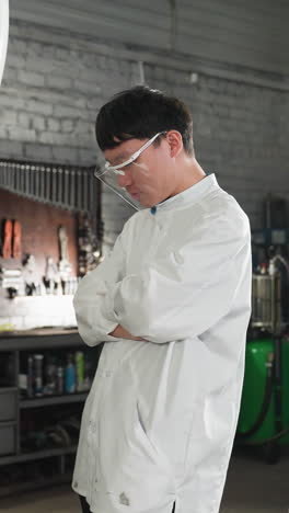 inventor en bata de laboratorio tomando una foto de un mecánico arreglando un neumático de coche mientras el estudiante observa con los brazos cruzados en el taller de mecánicos, herramientas en el fondo