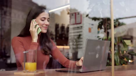 hermosa mujer de negocios hablando por teléfono móvil y trabajando en una computadora portátil sentada en una cafetería. dama sonriente hablando por teléfono inteligente con colegas o socios comerciales. retrato en primer plano hermosa mujer freelance