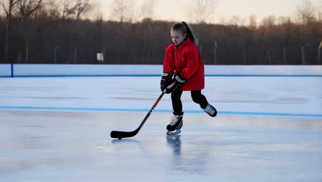 young girl ice skating and playing hockey on an outdoor ice rink