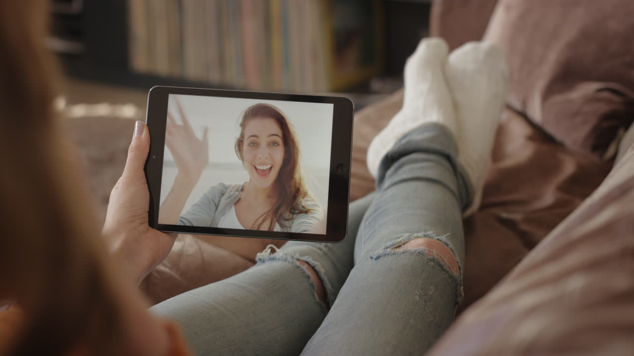 mujer feliz saludando a un amigo de vacaciones en casa a través de video de internet usando una aplicación de tableta digital en el sofá