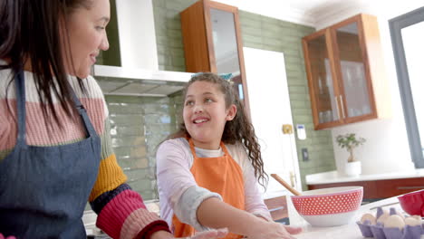 madre y hija bi-raciales felices poniendo masa en la lata de pastel y sonriendo en la cocina soleada