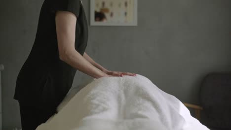 professional massage therapist placing hands on client's back who is lying on table covered with towel