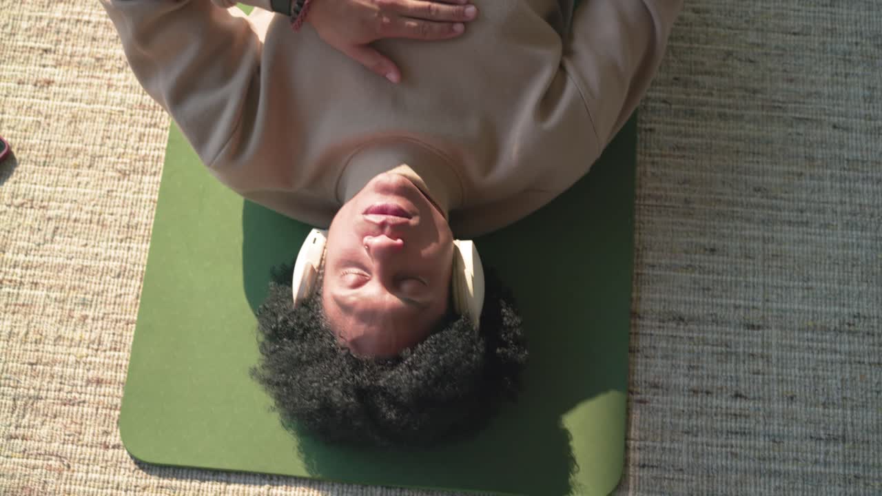 Smartphone aparecendo na borda esquerda, com a câmera dando zoom em um homem deitado em um colchonete verde meditando