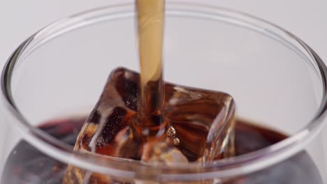 cerca de cola fresca que se vierte en el vaso con cubos de hielo en fondo blanco