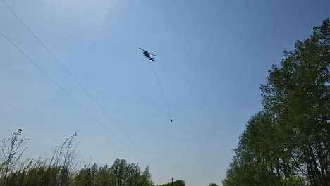 disparo de seguimiento de un helicóptero volando a través del cielo mientras lleva algo a través de un cable largo y lo deja en una fuente de agua