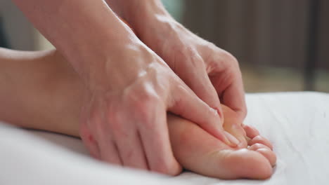 Close-up view of therapist using both thumbs to apply gentle pressure on client foot and side, focusing on technique, muscle tension release, and soothing care in peaceful massage room environment