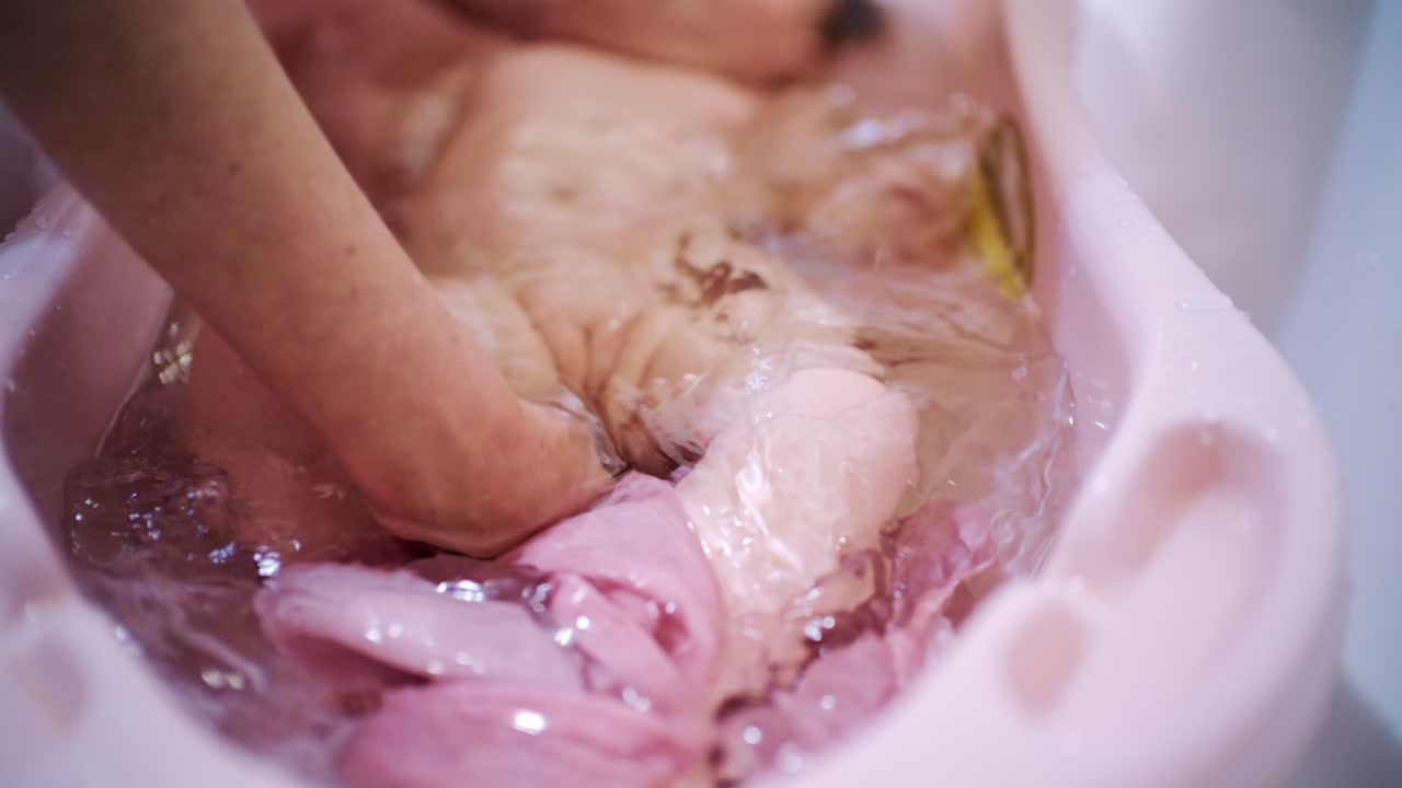 Neonato che fa il bagno in una vaschetta per neonati mentre un adulto lo sostiene e lo lava delicatamente