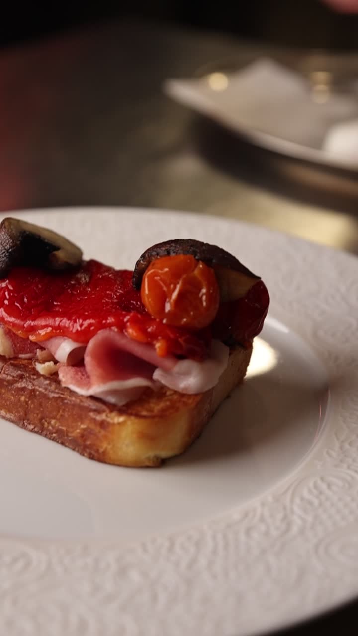 Mani che posizionano pomodoro arrosto su toast gourmet con prosciutto e peperoni