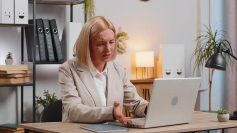 annoyed mature businesswoman looking at laptop screen irritated working remotely at office home