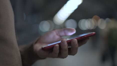 close-up of man's hand texting message on his smart phone with bokeh backdrop