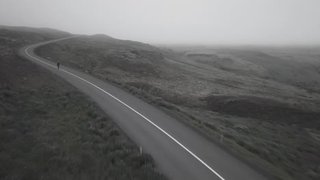 drone shots of skater going downhil on curvy road in a foggy, dramatic landscape in iceland