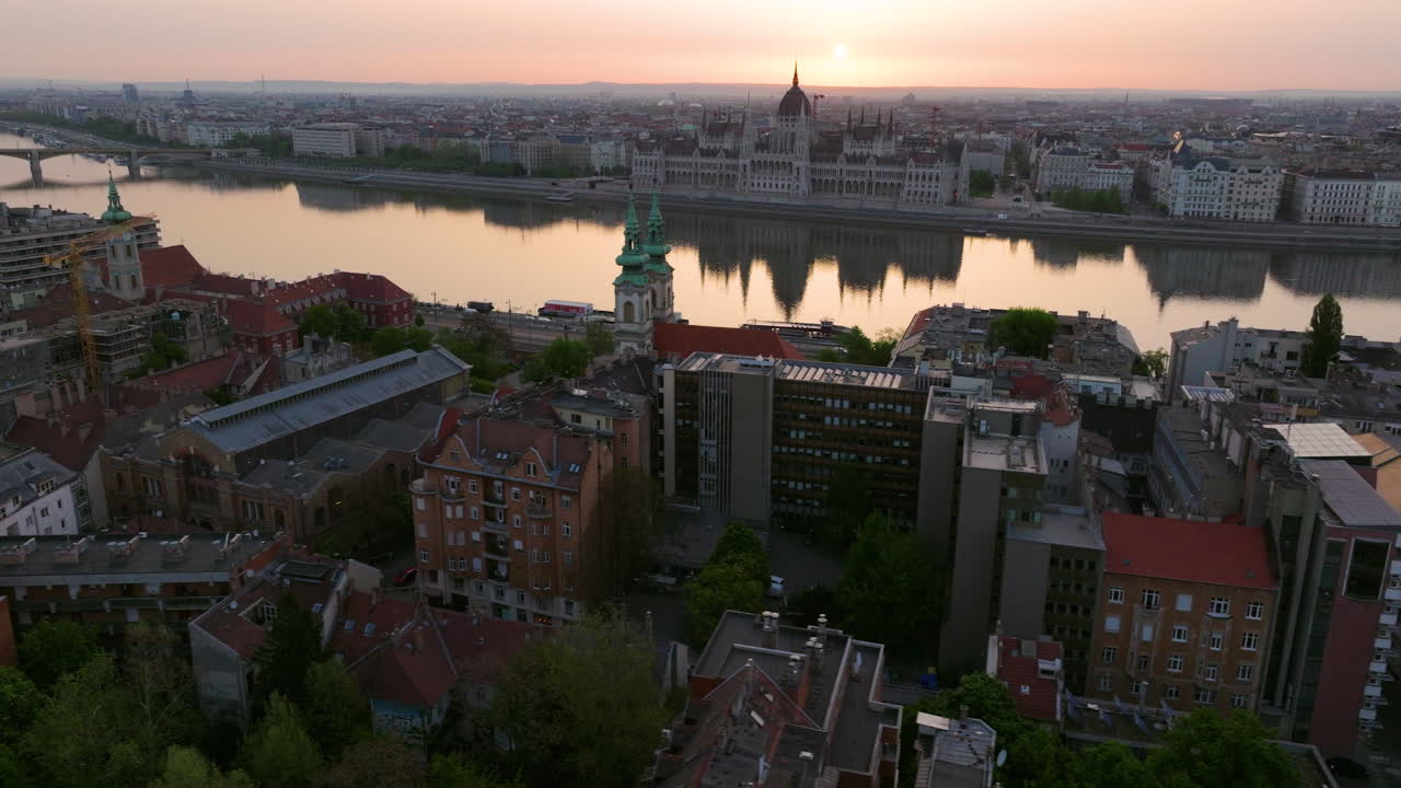 Catholic Church Opposite Hungarian Parliament Building With Reflections On Danube River At Sunrise. aerial sideways shot