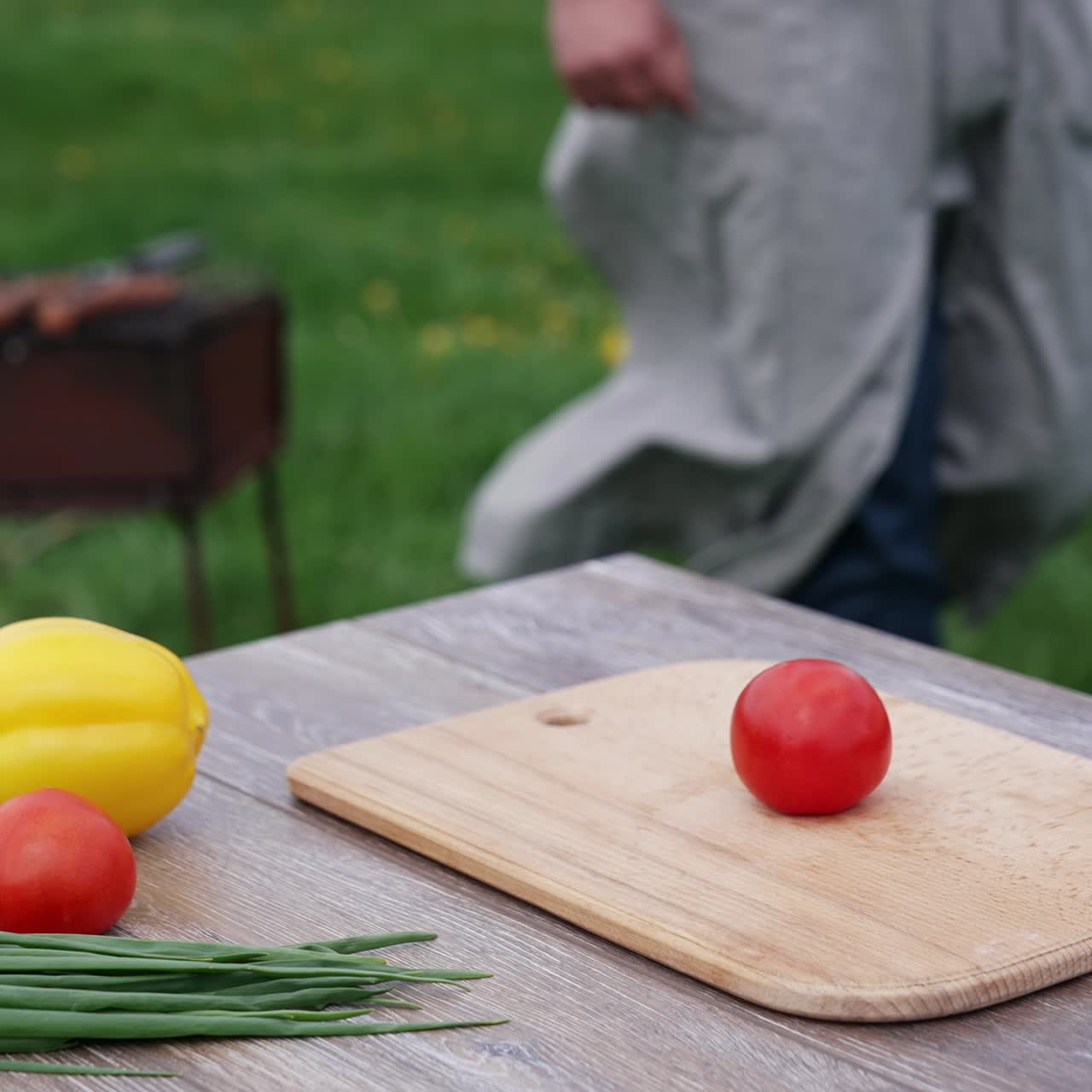 Fresh vegetable on the table in the open air. Tomatoes, cucumbers, onion and pepper on table on the background of a man cooking sausages on grill