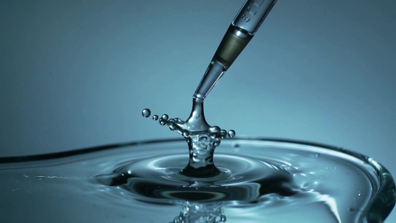 Releasing marked pipette tip dispensing droplet onto water in studio setup, forming crown ripples