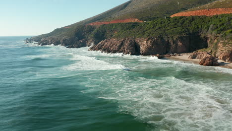 waves splashing on rugged cliffs at kogel bay beach, cape town, south africa - aerial drone shot