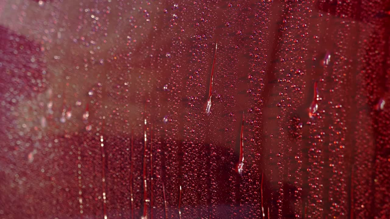 Extreme close up of water spray creating beads and rolling down dark cherry red car paintwork in the sun