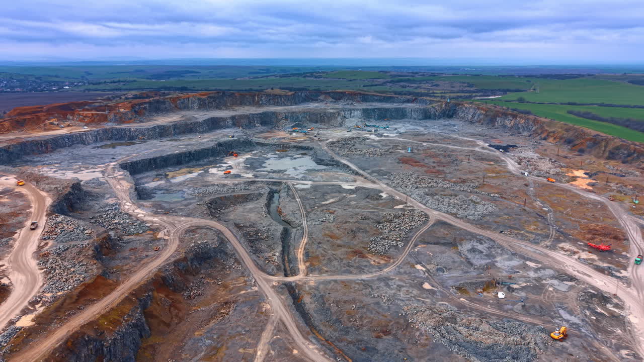 Industrial landscape of large open pit stone quarry with machinery. Wide aerial shot of stone mine showing excavation terraces, trucks, diggers, and dirt roads