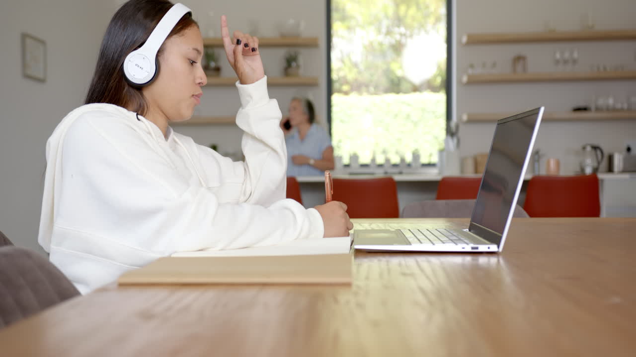 Studying at home, girl with headphones taking notes while using laptop