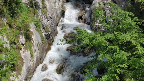 aéreo: vuelo hacia atrás alejándose de la cascada boka que fluye a través de rocas ásperas y terreno inaccesible