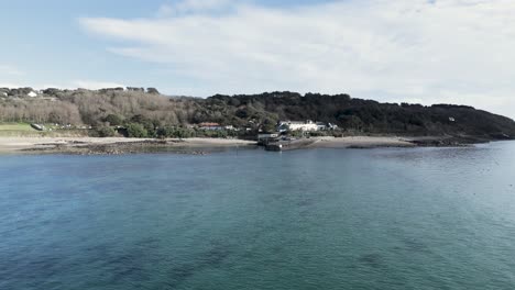 Niedriger-Anflug-über-Das-Meer-Zur-Herm-Island,-Kanalinseln,-über-Ruhiges-Meer-Zum-Strand-Und-Anlegesteg-Mit-Dem-Whitehouse-Hotel