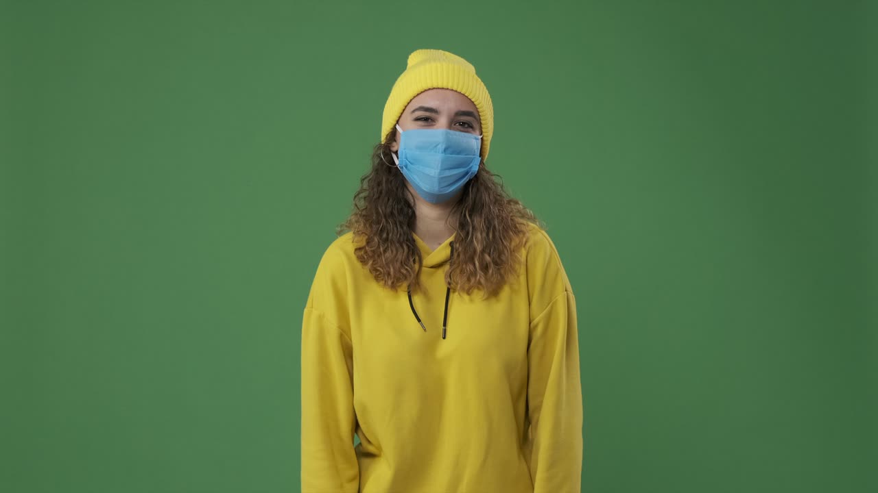 보호 얼굴 마스크를 착용 한 여성이 녹색 화면에서 웃고 있습니다.