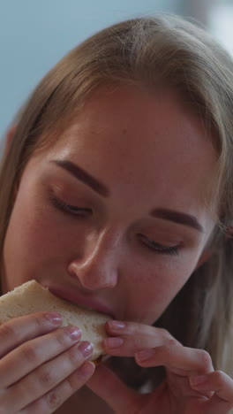 hungry blonde woman bites delicious sandwich with cheese on blurred background. young student enjoys snack after doing homework closeup