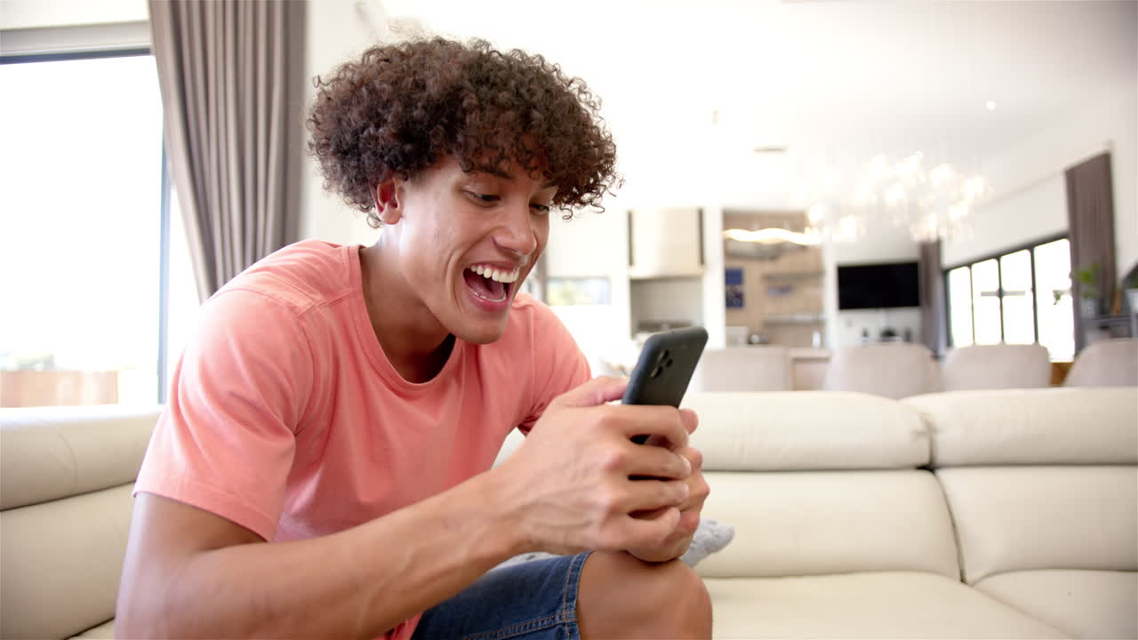 Smiling man using smartphone while sitting on couch in modern living room