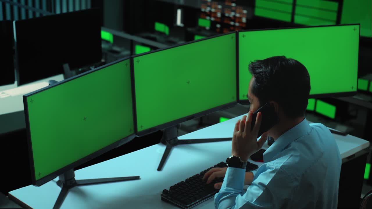 vista lateral de un hombre asiático hablando en teléfono móvil mientras trabaja con múltiples monitores de computadora simulados en la oficina