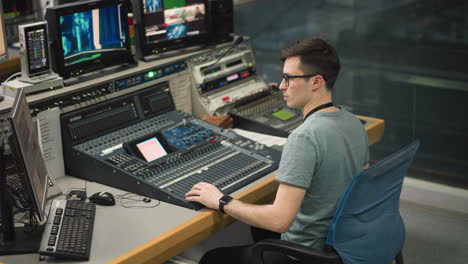 broadcast operator managing mixing console and monitors in control room, focused on adjusting sound levels for live production. operator sitting in front of high-tech equipment handling broadcast tasks
