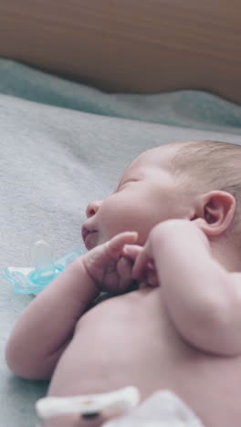 nice newborn baby with short blond hair and pacifier in mouth wearing white diaper lies on changing table closeup