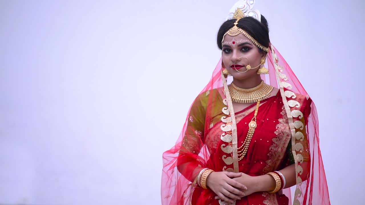 Isolert indisk bengalsk brud iført rød sari smiler mot hvit bakgrunn.