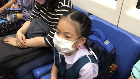 asian student child girl going to school in the morning, wearing a medical mask, taking subway or mrt of thailand