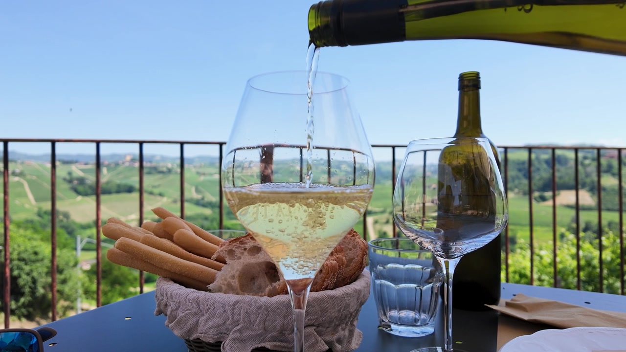 Versamento al rallentatore di vino bianco in un bicchiere con antipasti su una terrazza panoramica