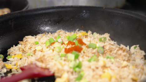 Sprinkling-masago-over-green-onion-topped-crab-fried-rice-in-hot-pan-over-stove,-close-up-slow-motion-4K